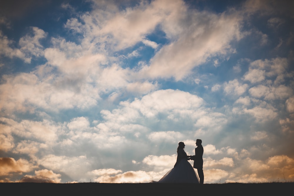 a bride and groom standing under a cloudy sky