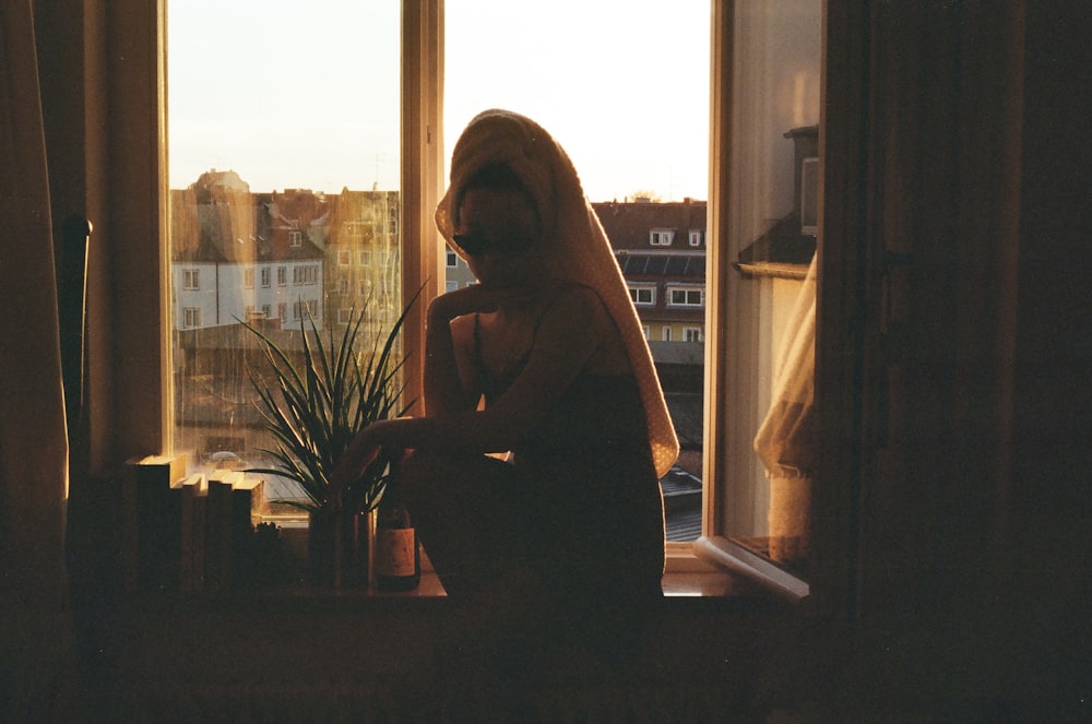 a woman standing in front of a window next to a potted plant