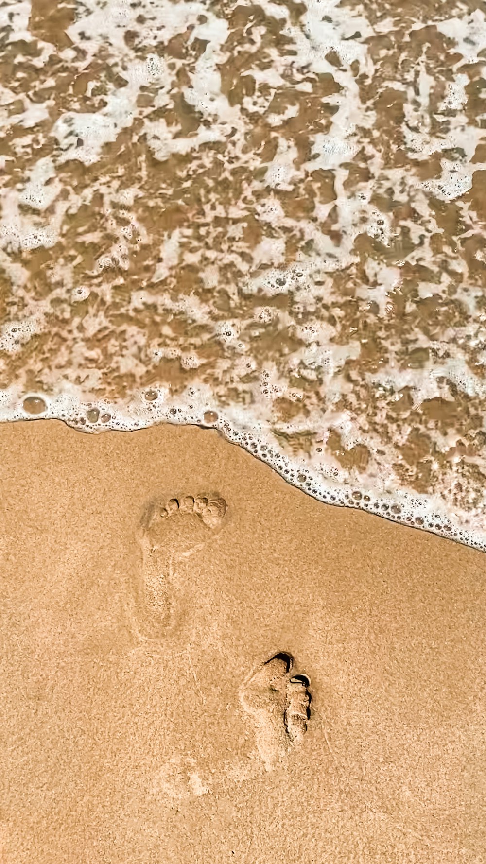 a person's footprints in the sand next to the ocean