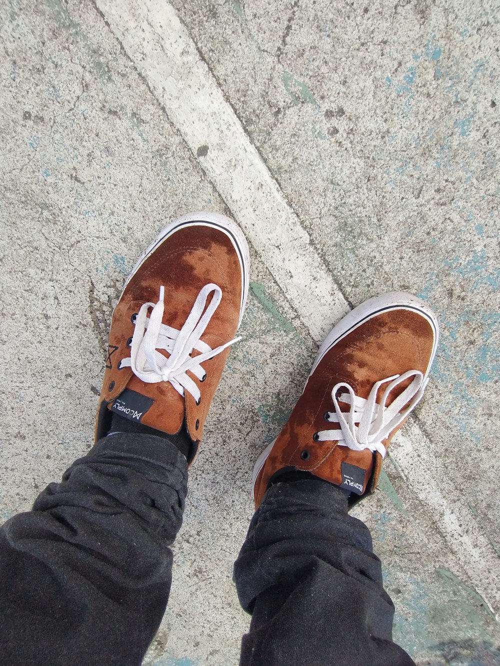 a person wearing brown shoes standing on a sidewalk