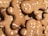 Gingerbread cookies shaped like people with icing decorations are stacked together. The cookies feature simple designs with dots and curved lines representing facial features and buttons. The texture of the cookies appears crisp and lightly browned.