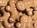 Gingerbread cookies shaped like people with icing decorations are stacked together. The cookies feature simple designs with dots and curved lines representing facial features and buttons. The texture of the cookies appears crisp and lightly browned.