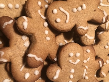 Gingerbread cookies shaped like people with icing decorations are stacked together. The cookies feature simple designs with dots and curved lines representing facial features and buttons. The texture of the cookies appears crisp and lightly browned.