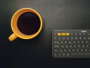 Close-up of hands typing on a laptop with a black and yellow coffee mug nearby.