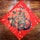 A decorative piece of art features intricate gold and black designs on a red square, possibly depicting stylized clouds and abstract Chinese characters. The artwork is set against a wooden background.