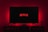 A dark room featuring a television screen displaying the word 'Netflix' in red against a black background. The screen is centered on a console table, with a video game controller placed in front. The room is dimly lit by red ambient lighting, creating a cozy atmosphere.