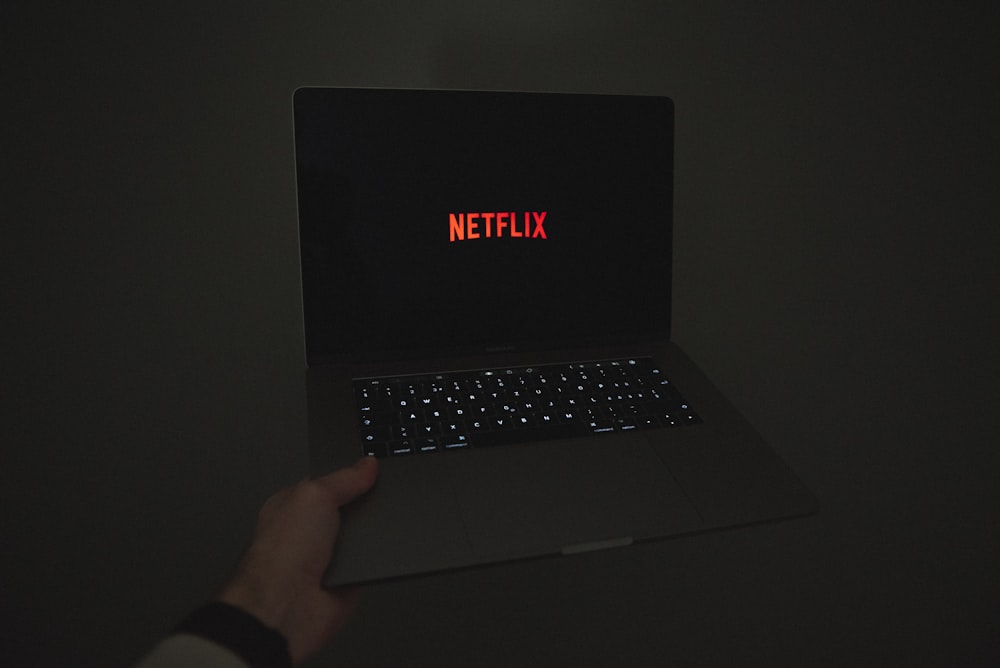a person holding a laptop with the word netflix on the screen