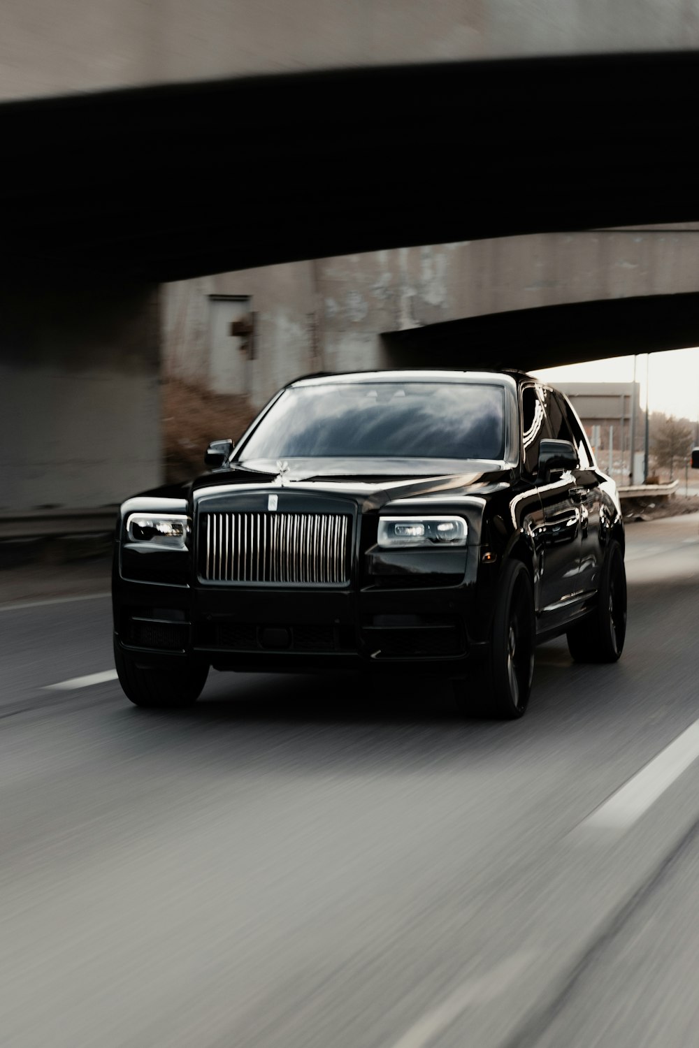 a black truck driving down a street under a bridge