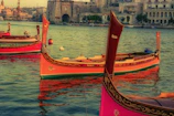 Colorful traditional Maltese fishing boats bobbing in the clear blue harbor.