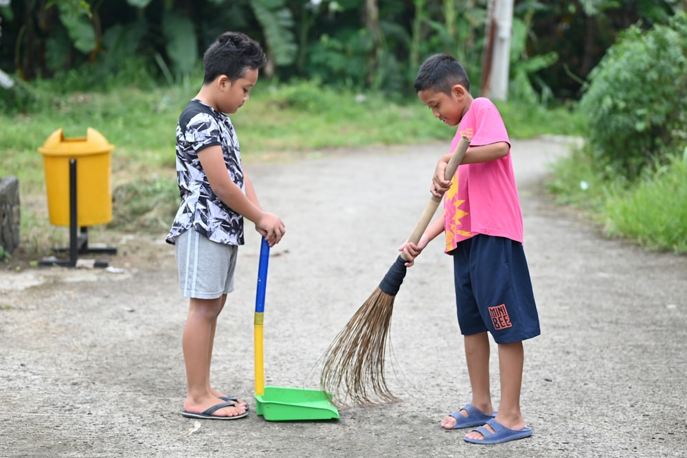 two young boys with brooms on a dirt road