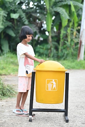 a little girl standing next to a yellow trash can