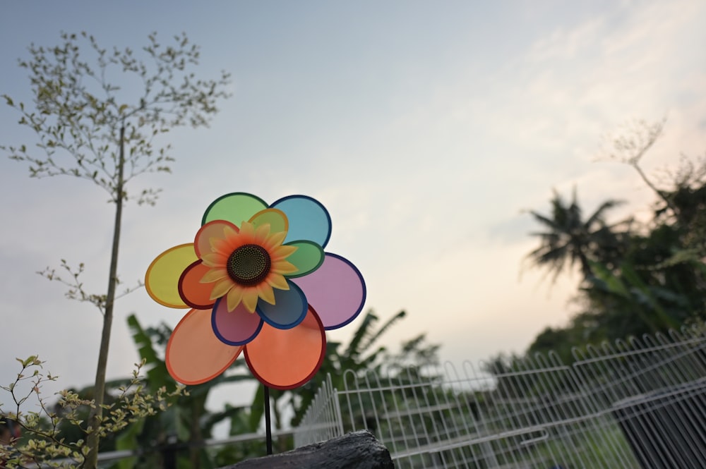 a multicolored flower shaped wind spinner in front of a fence