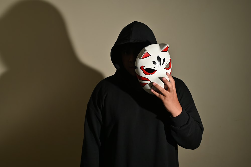 a man in a black hoodie holding a white mask