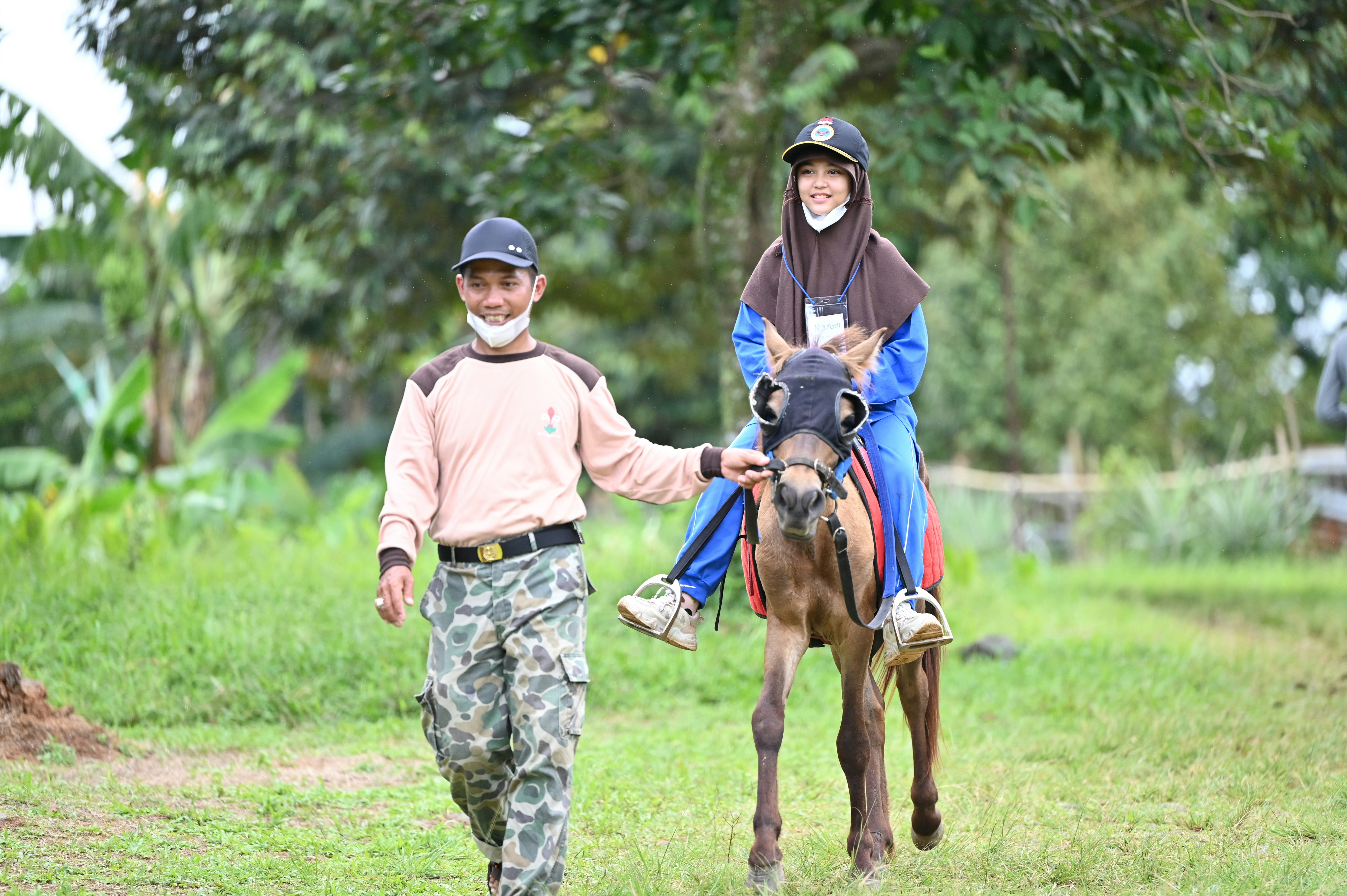 Zwei Personen gehen mit einem Pferd auf einem Feld spazieren