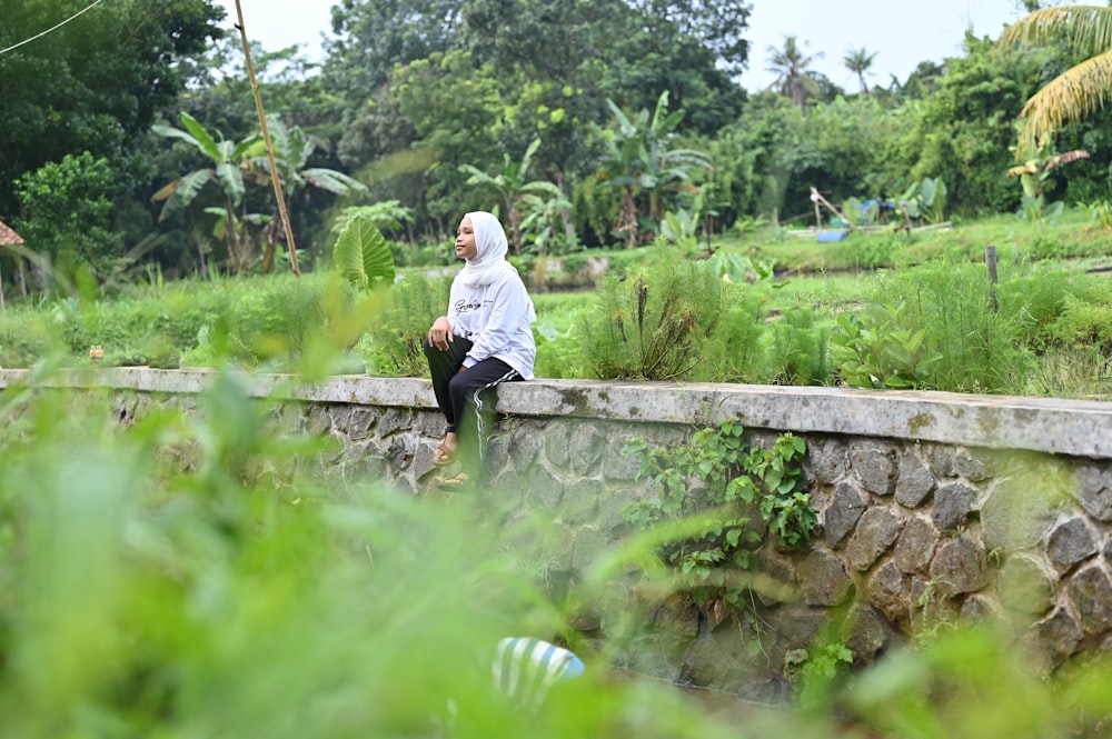 a woman sitting on a stone wall next to a lush green field