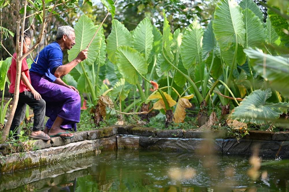 a man and a woman sitting on a rock next to a pond