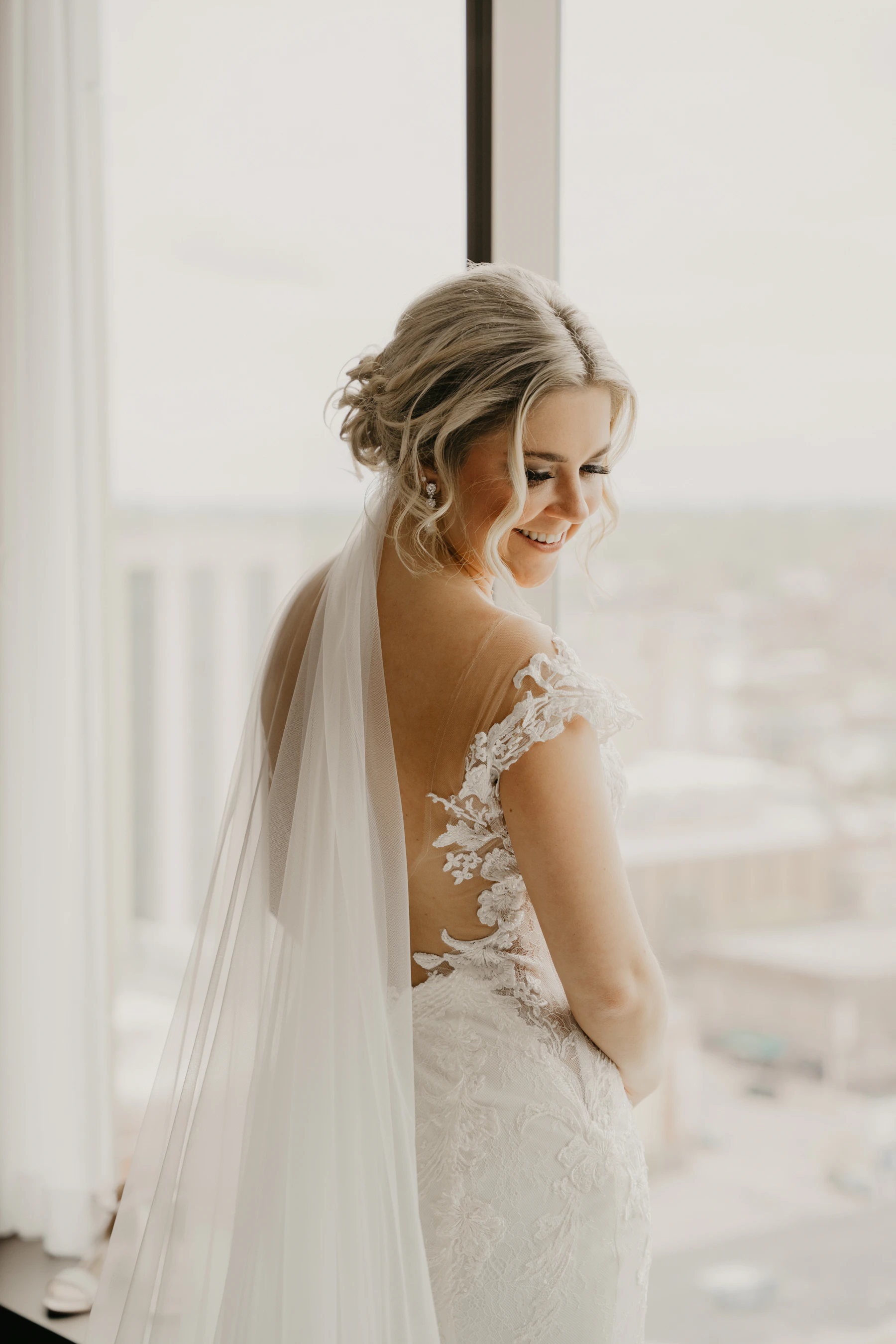 A bride in her wedding dress looking out a bright window