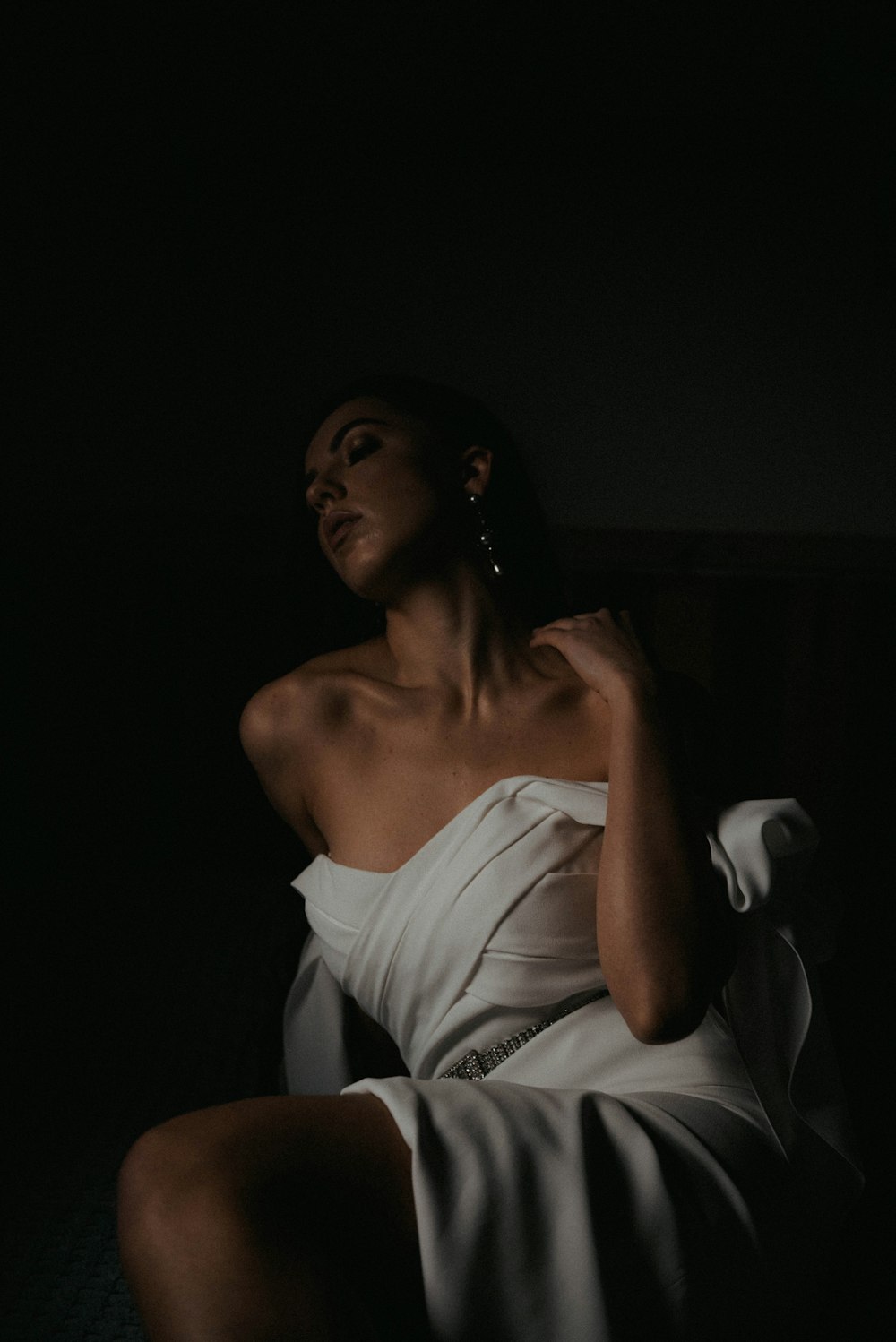 a woman in a white dress sitting in the dark