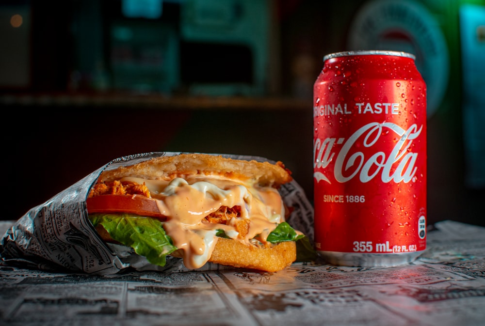 a can of soda and a sandwich on a table