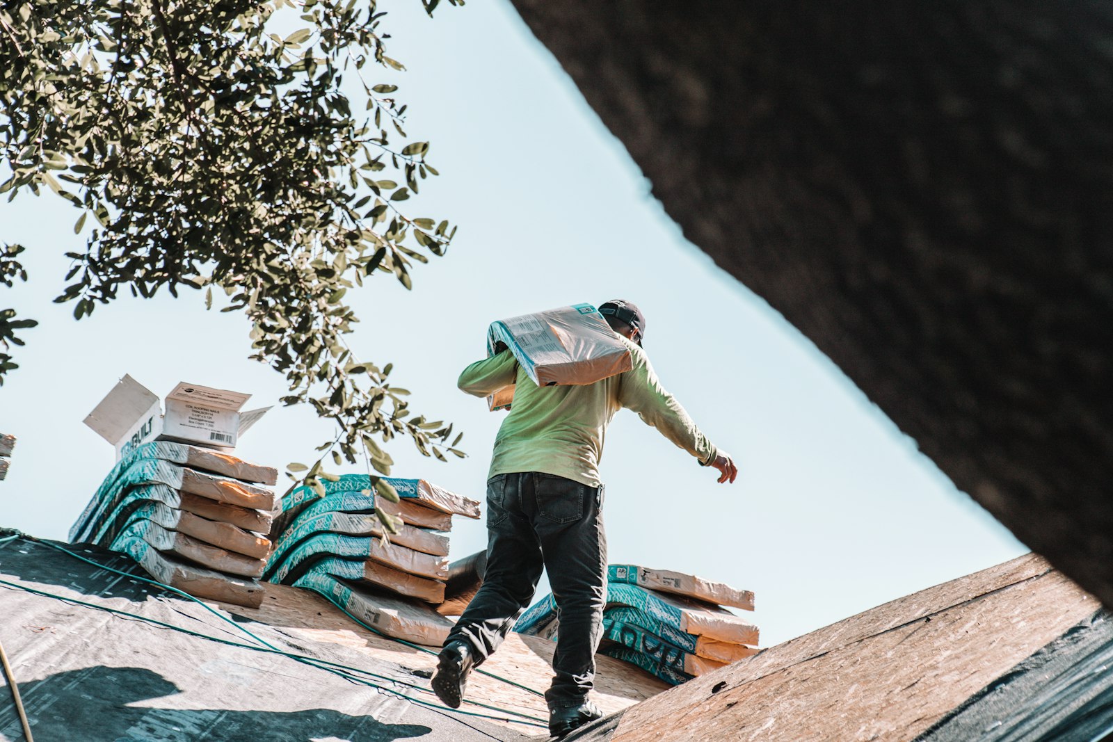 Roofer carrying shingles across a residential roof against a clear sky