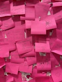 A collection of pink sticky notes, each with handwritten messages and doodles. The notes contain encouraging phrases, expressions of love, and quirky drawings. The notes are layered on top of each other, creating a vibrant and cluttered composition.