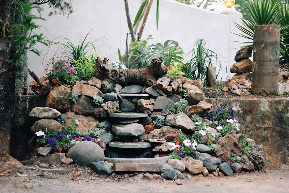 a fountain surrounded by rocks and flowers in a garden