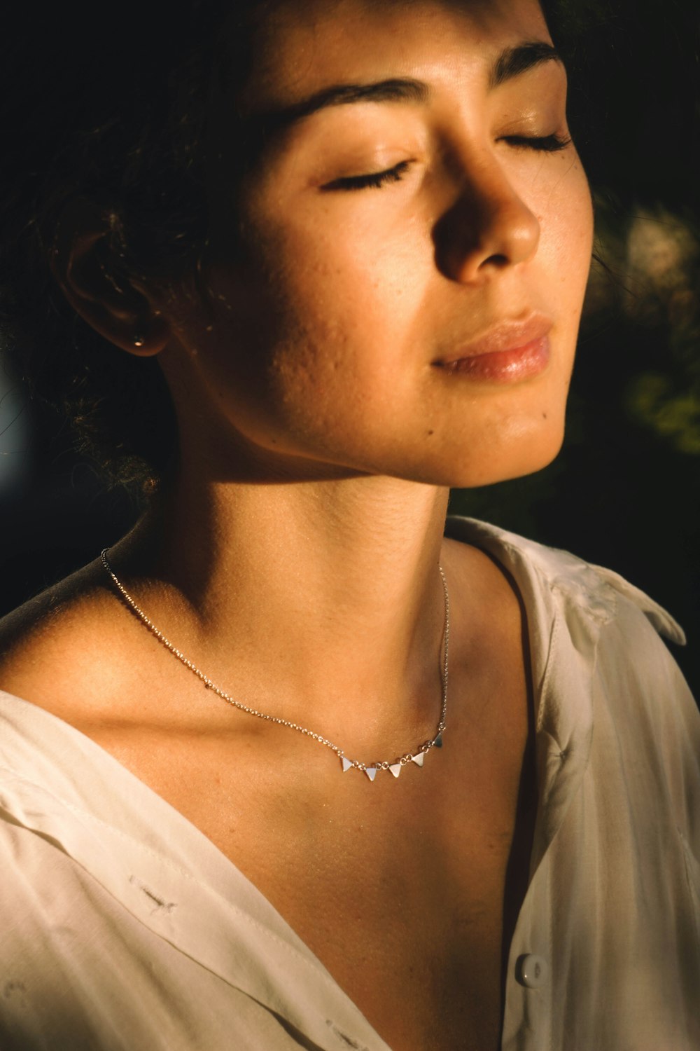 a woman with her eyes closed wearing a necklace