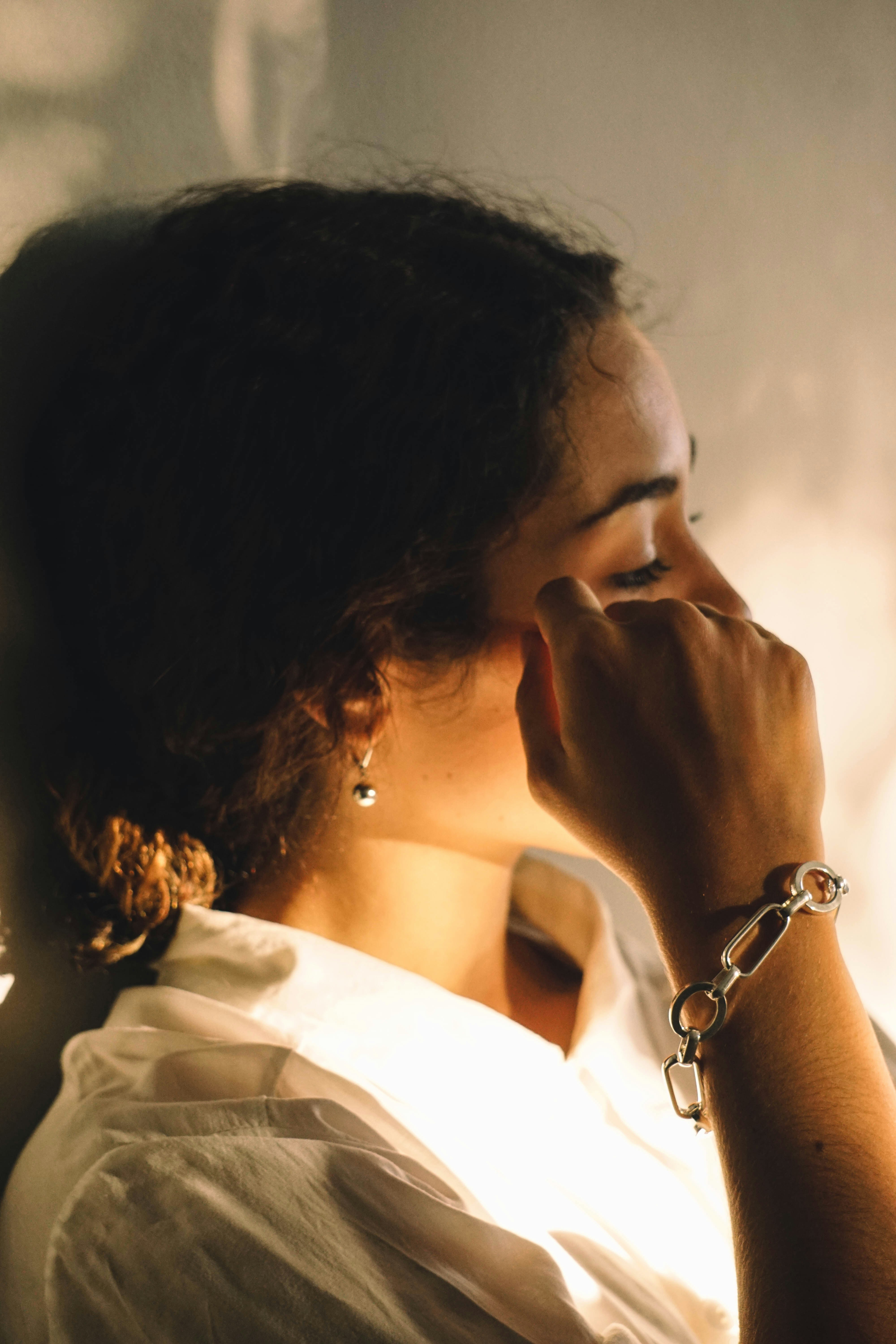 a woman in a white shirt is holding her hand up to her face