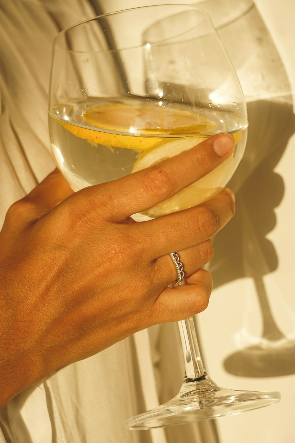 a person holding a glass of wine with a slice of lemon in it