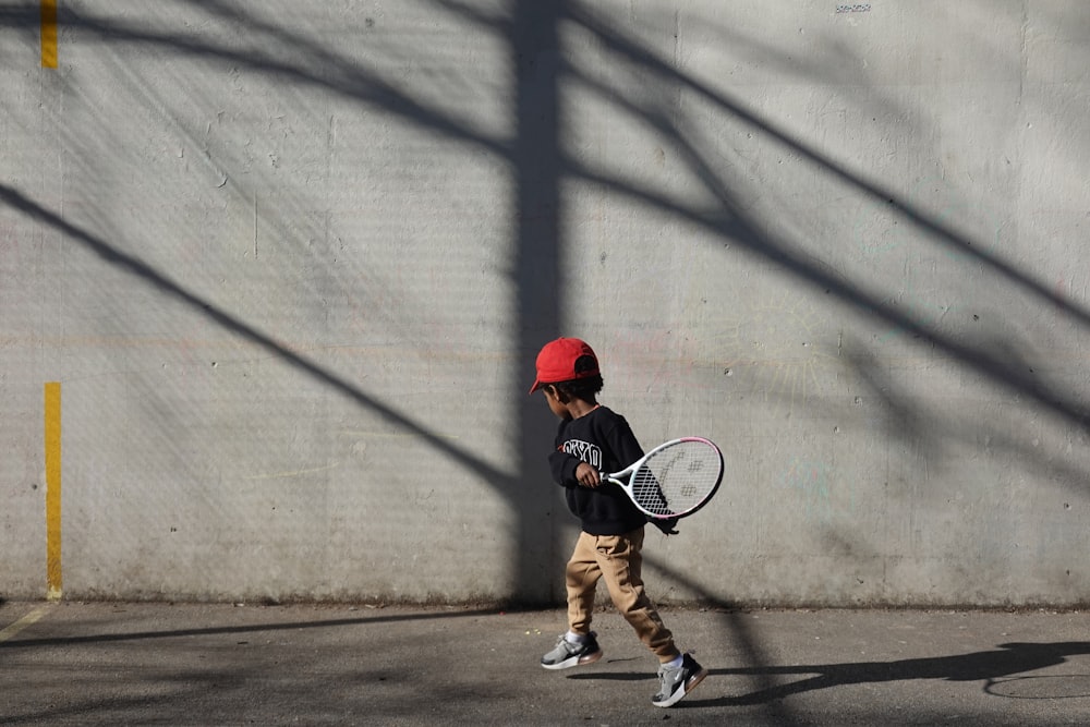 Un giovane ragazzo che cammina lungo una strada con in mano una racchetta da tennis