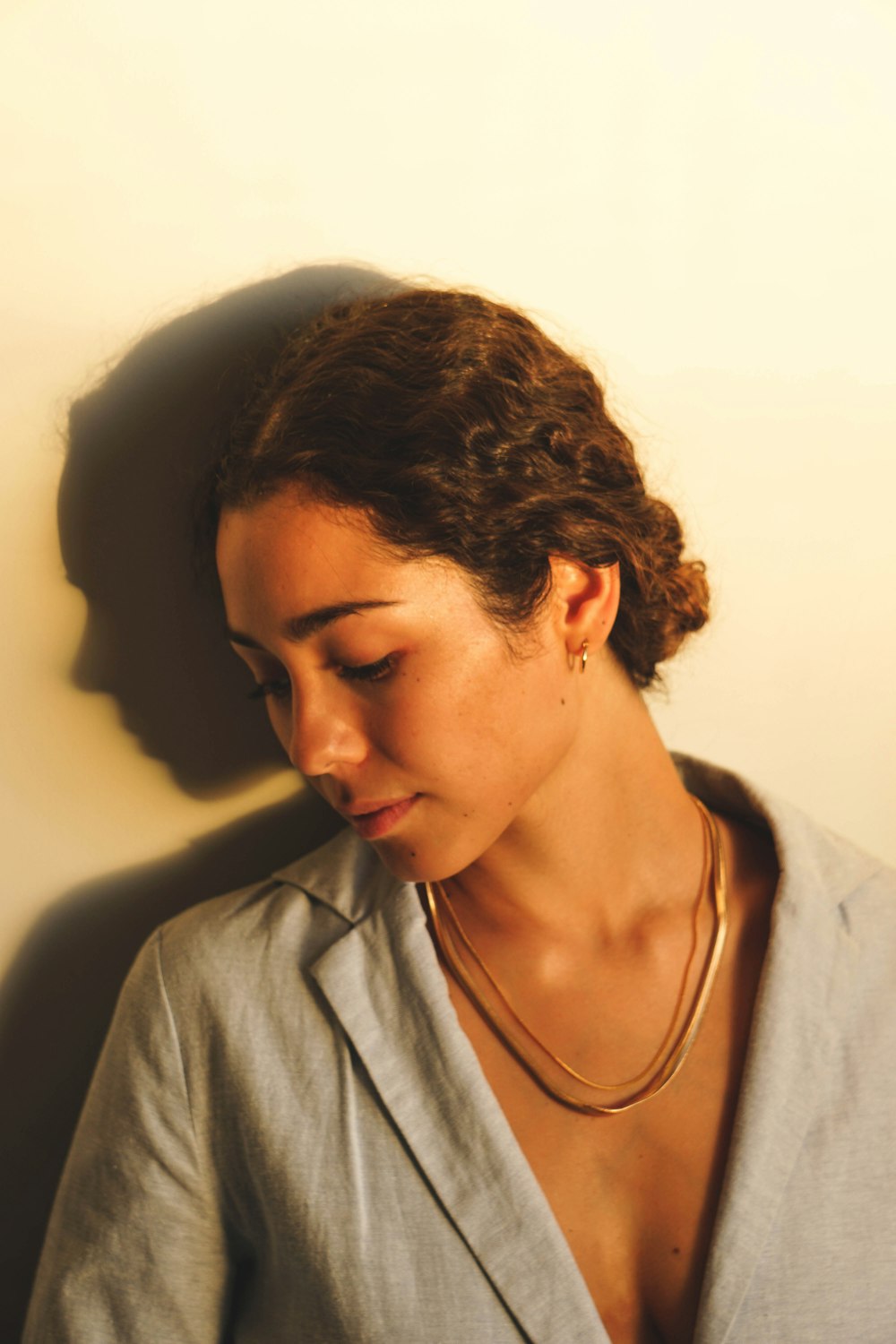 a woman with a necklace on her neck leaning against a wall
