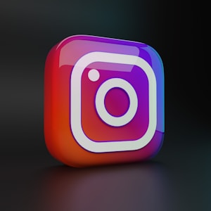 A glossy 3D icon with the Instagram logo. The icon is in a cube shape with rounded edges, displaying vibrant gradient colors blending from red and orange to purple and blue. The logo is white and set against a dark background, creating a striking contrast.