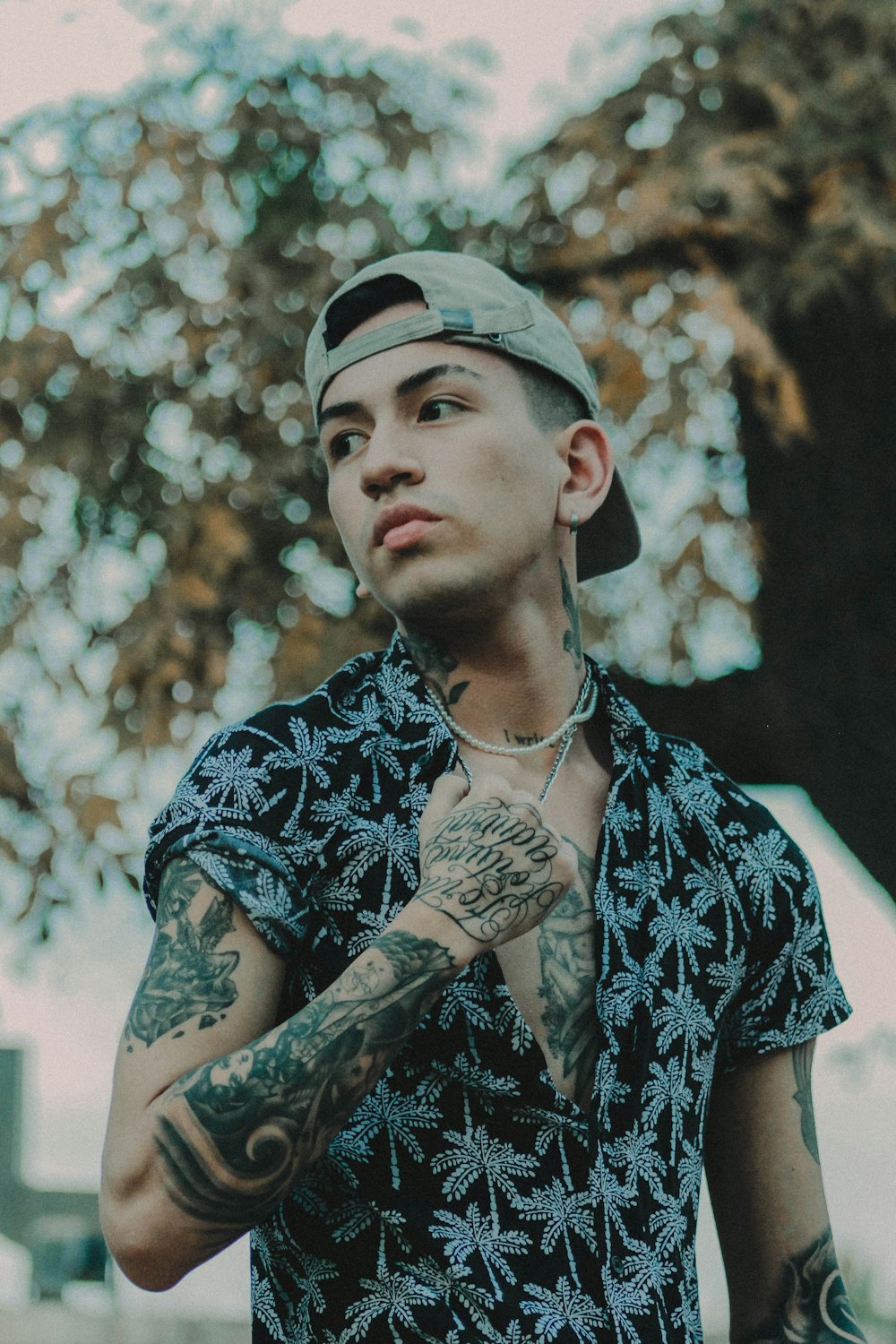 a man with tattoos standing in front of a tree