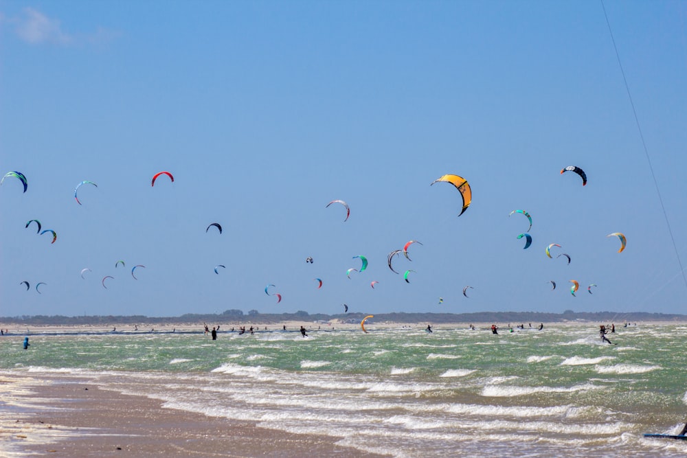 a group of people flying kites on top of a sandy beach