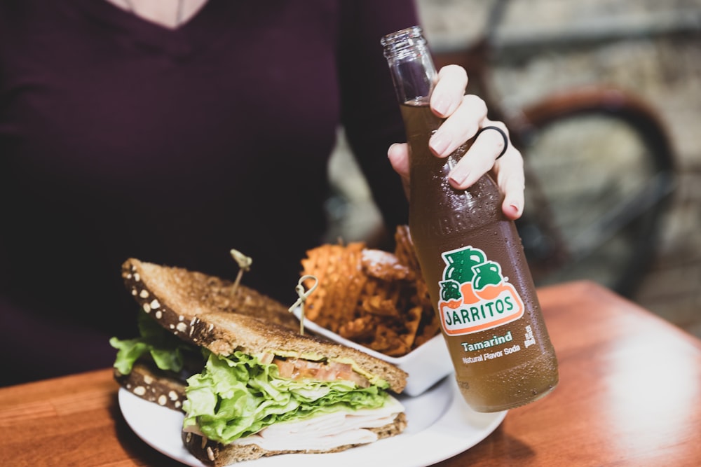 a woman holding a bottle of beer and a plate of food