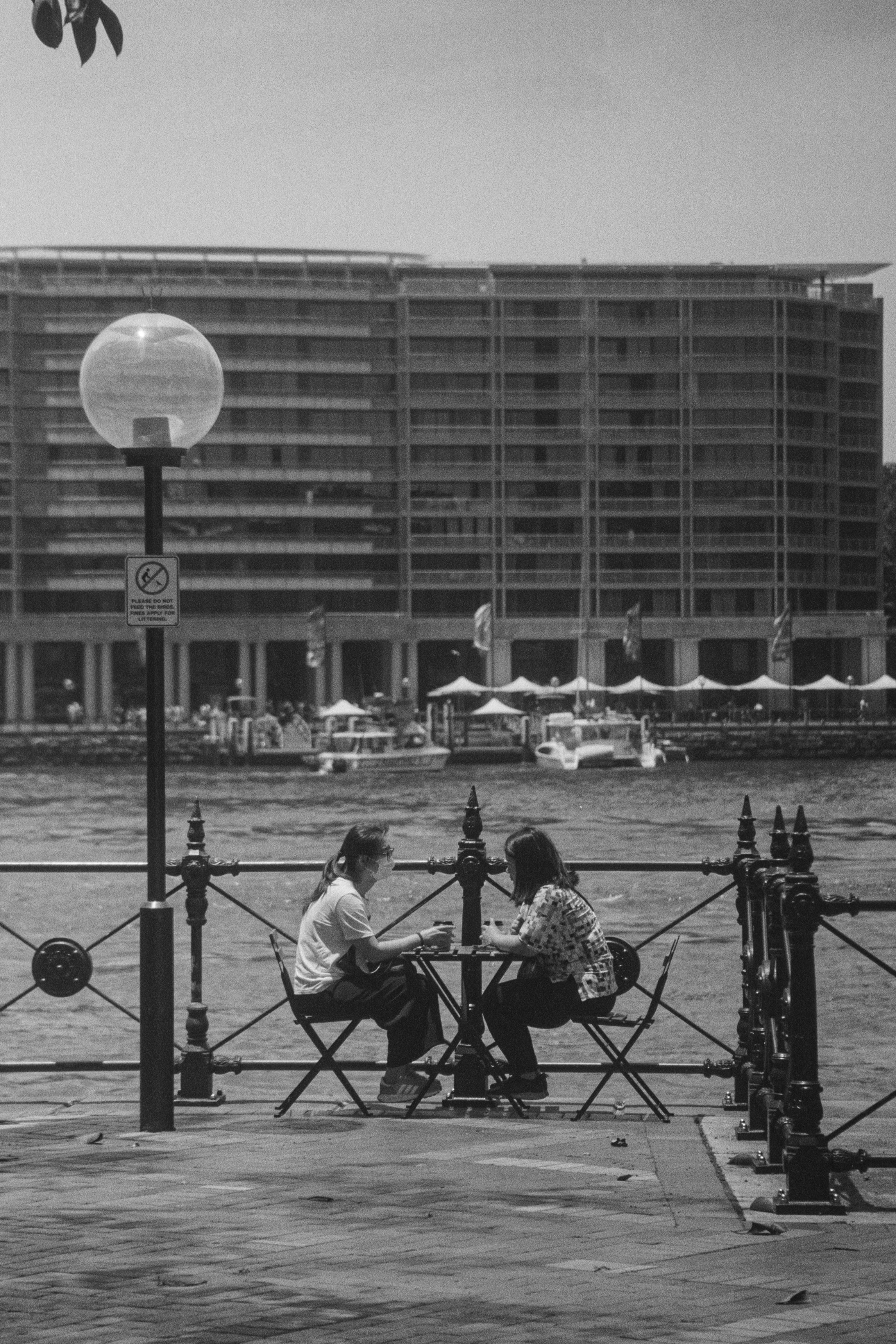 A couple of people sitting on a bench next to a body of water photo ...
