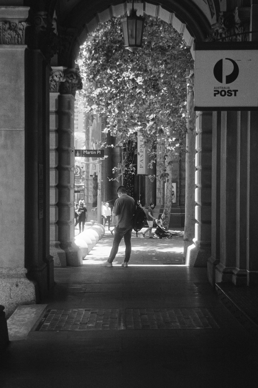 a man walking down a sidewalk under an arch