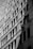 Two workers are suspended on ropes, cleaning the windows of a tall building. The geometric pattern of the windows creates a dynamic visual effect in black and white. The sunlight casts shadows that add depth to the image.