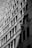 Two workers are suspended on ropes, cleaning the windows of a tall building. The geometric pattern of the windows creates a dynamic visual effect in black and white. The sunlight casts shadows that add depth to the image.