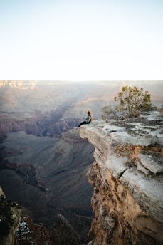 a man sitting on top of a cliff overlooking a canyon