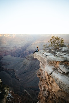 a man sitting on top of a cliff overlooking a canyon