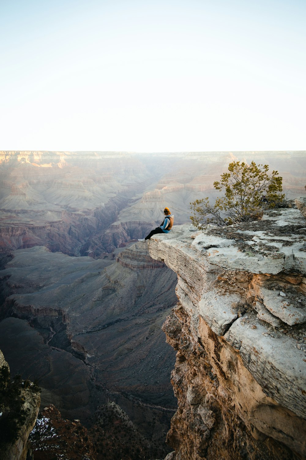 a man sitting on top of a cliff overlooking a canyon