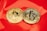 Two gold coins are placed on a glossy red surface, featuring the symbols for Bitcoin and Tezos. The coins are intricately designed with digital circuit patterns, symbolizing their status as cryptocurrencies.