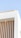 A minimalist building design with vertical wooden slats against a white textured wall. The structure features a modern architectural style with clean lines and a small light fixture on the undersurface. The sky is clear and blue in the background.