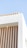 A minimalist building design with vertical wooden slats against a white textured wall. The structure features a modern architectural style with clean lines and a small light fixture on the undersurface. The sky is clear and blue in the background.
