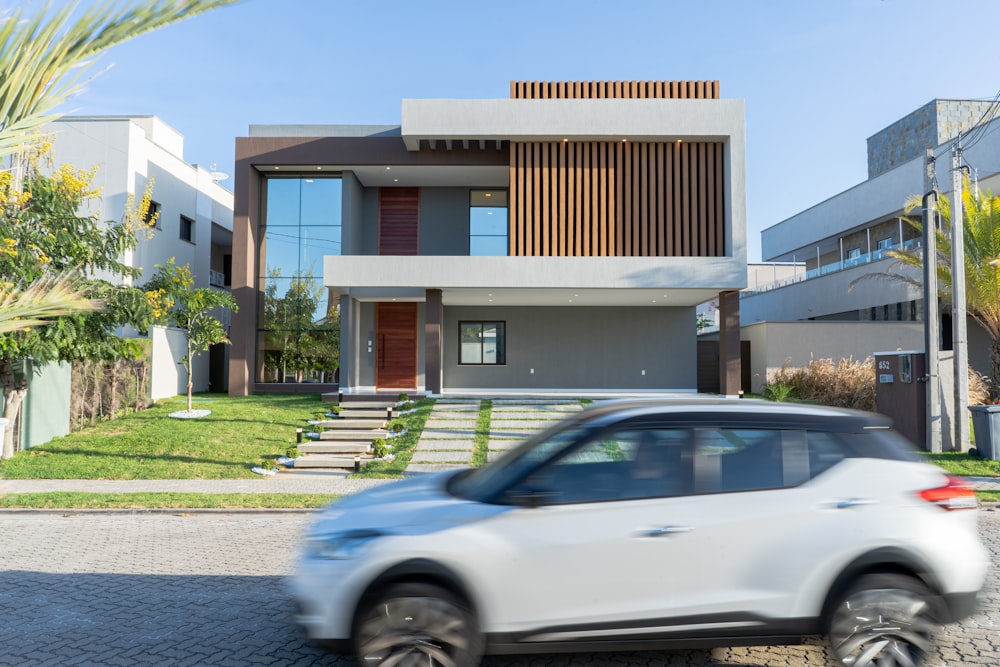 a white car driving past a modern house