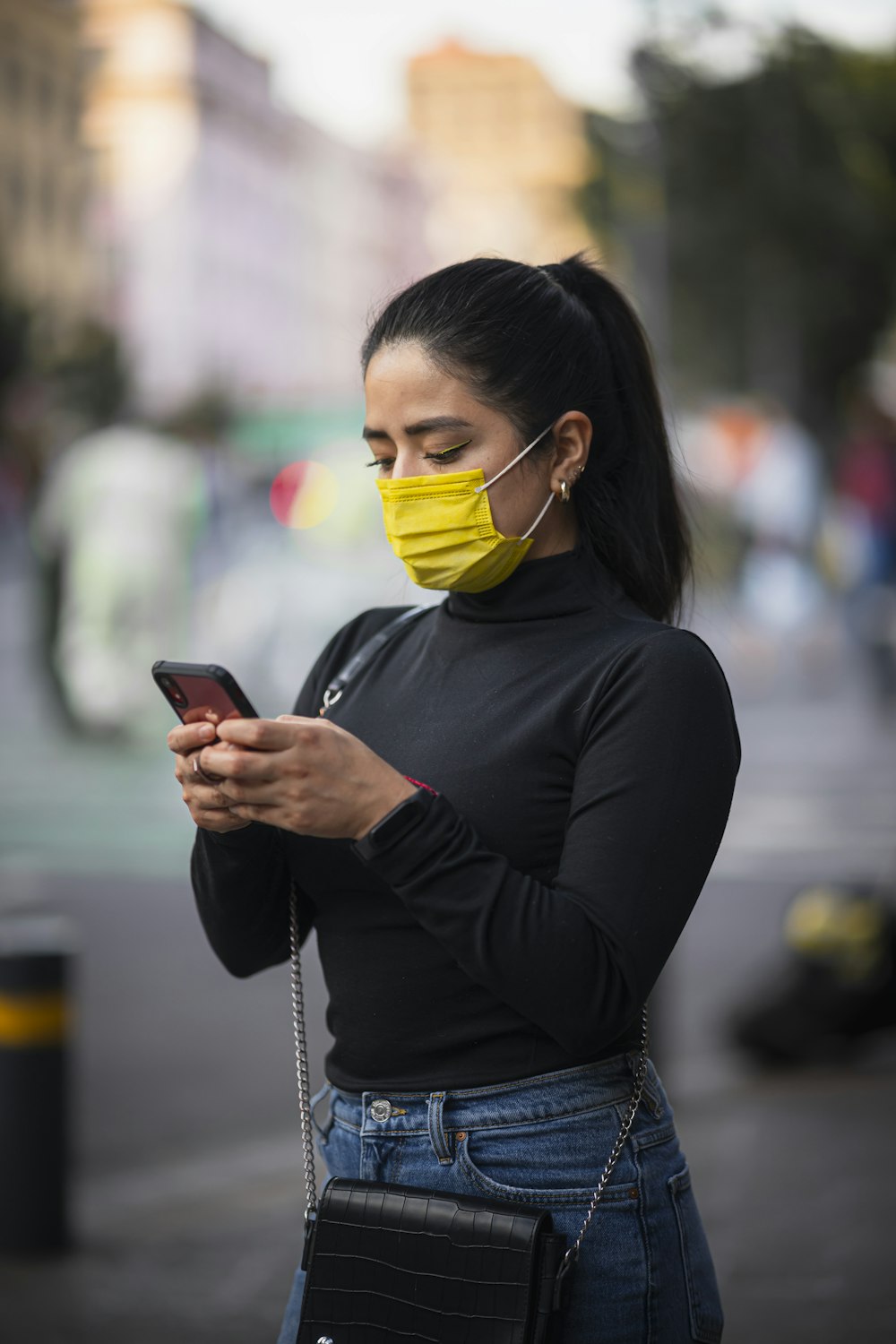 Une femme portant un masque facial tout en regardant son téléphone portable