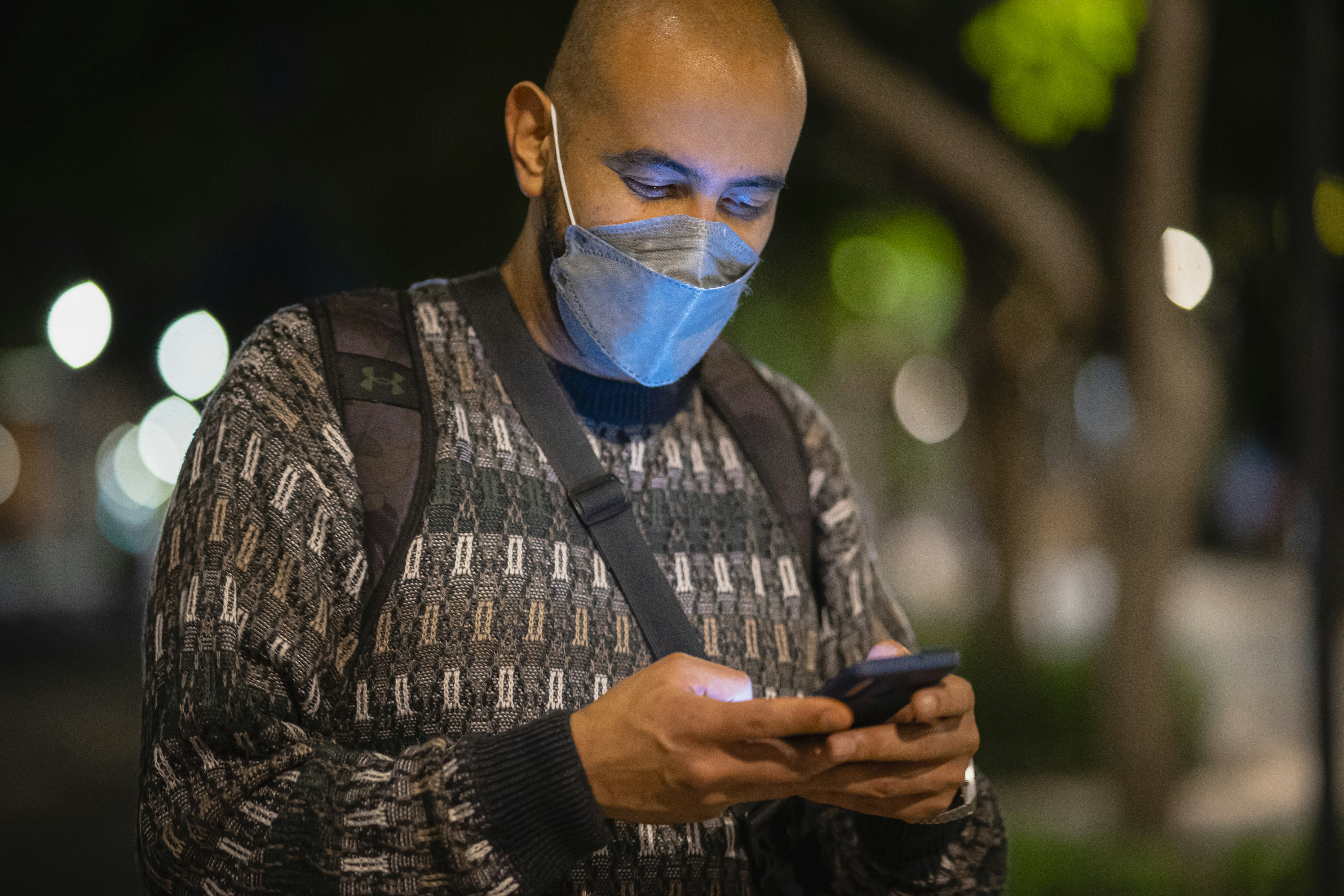 a man wearing a face mask looking at his cell phone