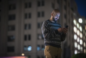 a man standing in front of a tall building looking at his cell phone