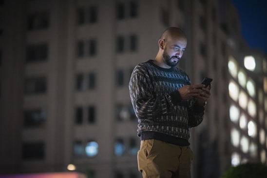 a man standing in front of a tall building looking at his cell phone